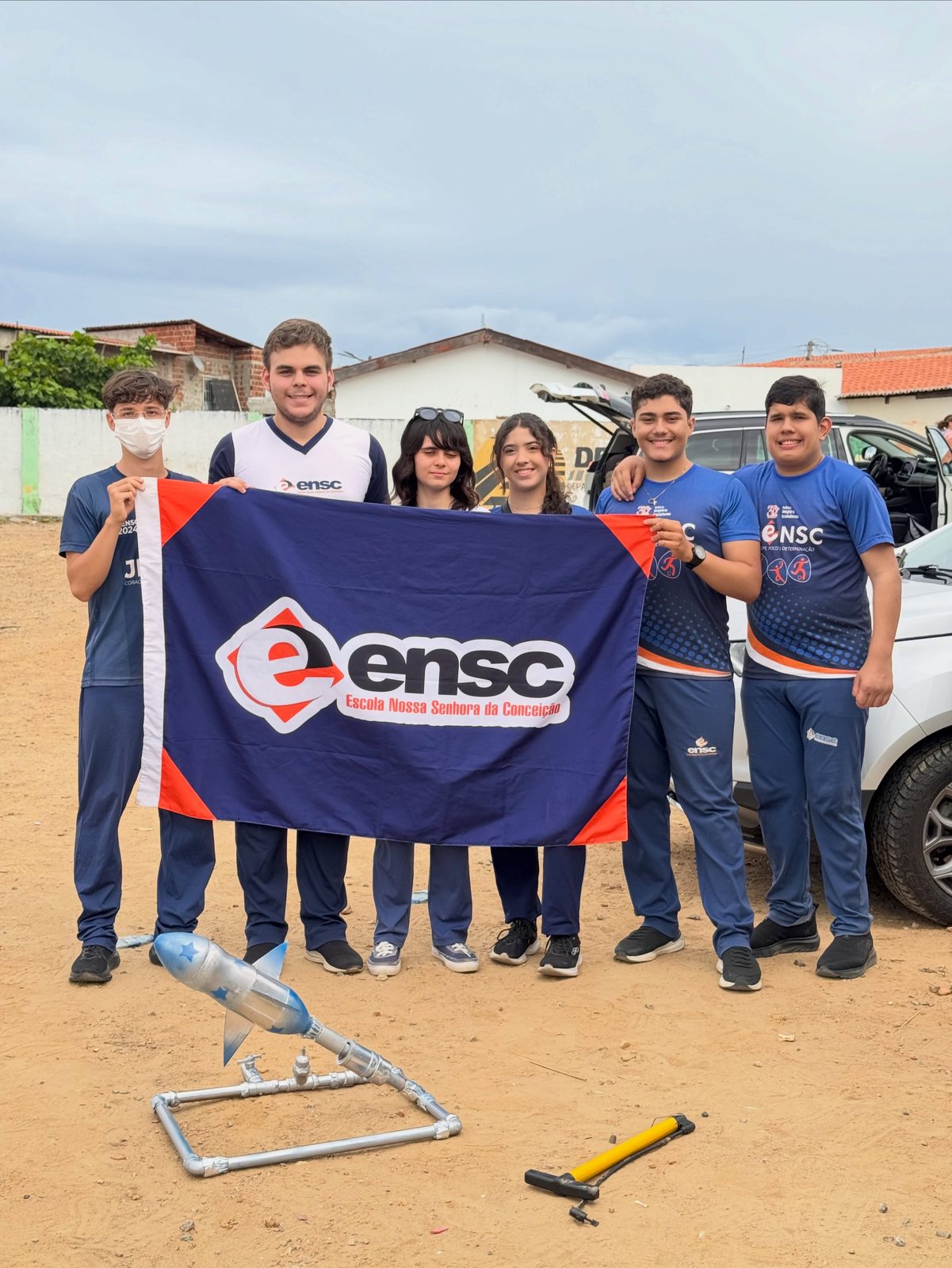 Equipe de alunos posa com a bandeira da ENSC e um foguete prateado